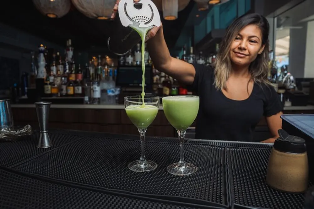 A bartender is pouring a green cocktail into a stylish glass with a smile