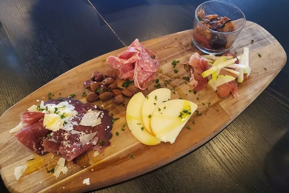 A charcuterie board is presented with a variety of meats cheese olives and garnishes arranged on a wooden serving platter