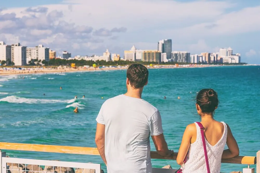 A couple is enjoying the view of a vibrant beachfront with surfers and skyscrapers in the background