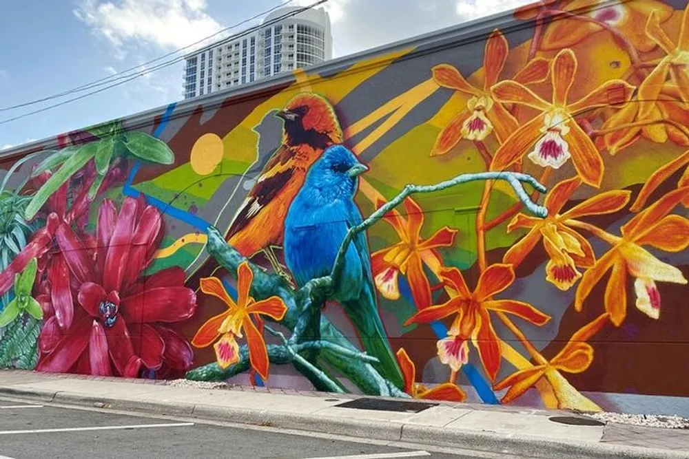 The image shows a vibrant street mural featuring oversized colorful birds and tropical flowers against an abstract background adding a splash of nature to an urban setting