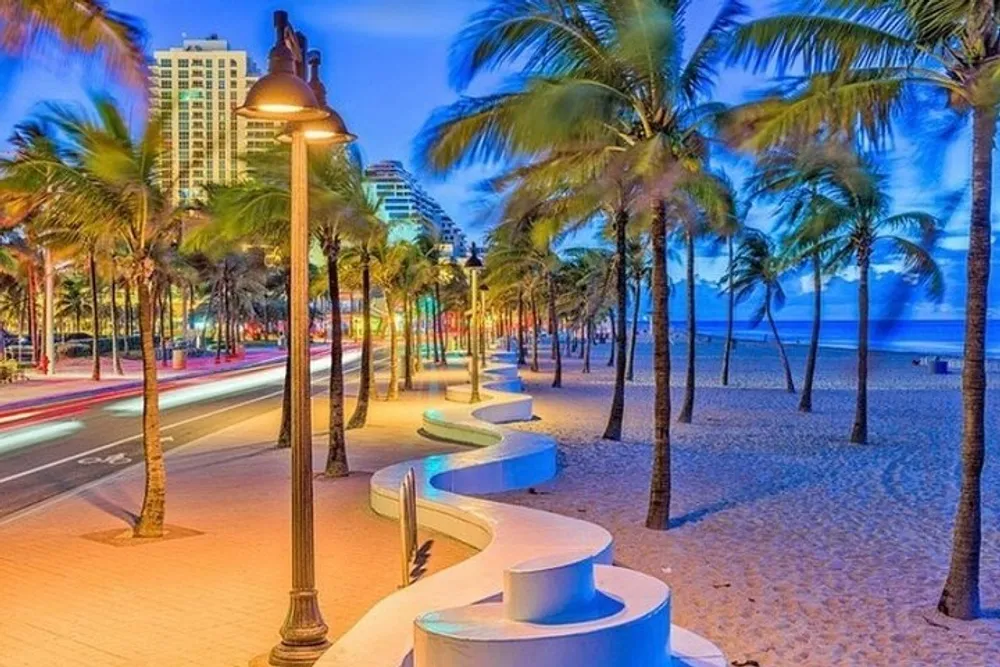 The image depicts a vibrant beachside walkway at twilight with illuminated street lamps palm trees and the blurred lights of passing traffic against a backdrop of ocean and skyscrapers