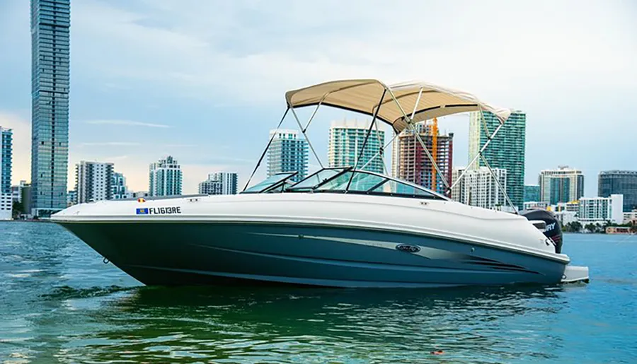 A motorboat is anchored near a city waterfront with skyscrapers in the background under a cloudy sky.