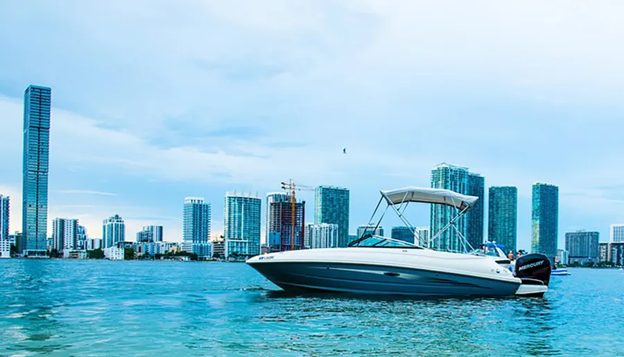 A powerboat is anchored near the coastline with a backdrop of modern skyscrapers under a light blue sky.