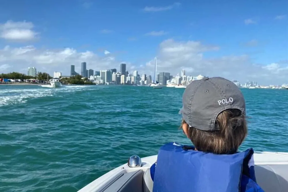 A person wearing a cap is looking at the skyline of a modern city from a boat on the water