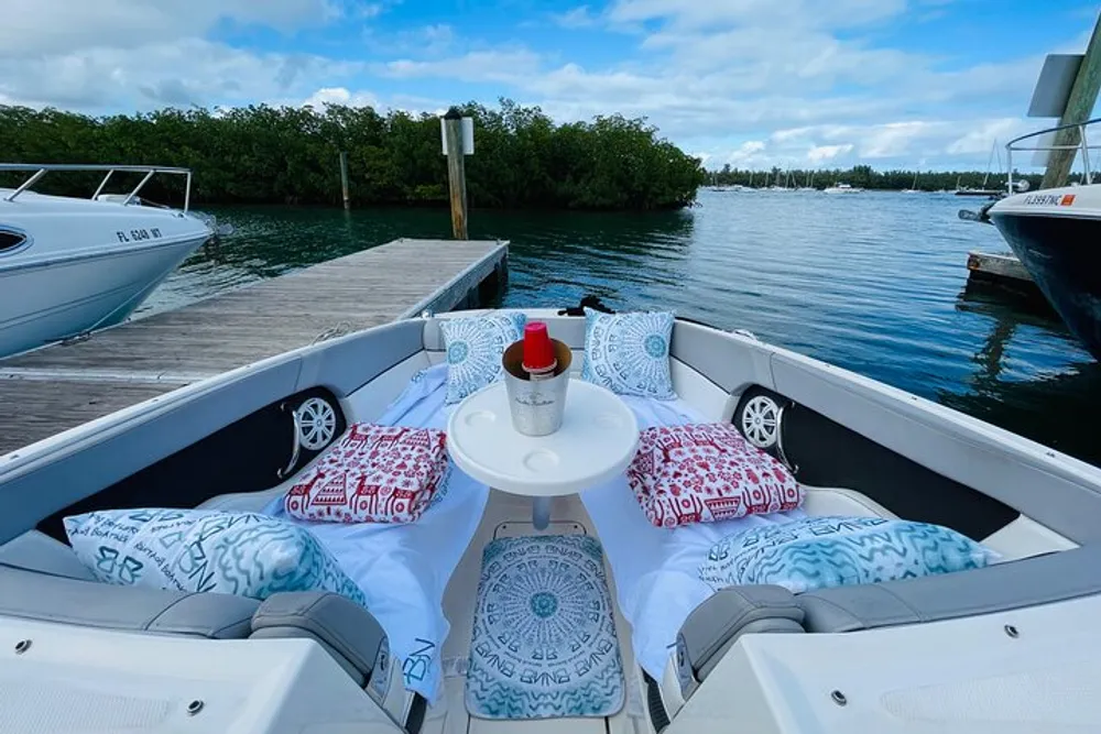 This image shows a comfortable seating area on a boat with cushions and a bottle docked at a pier with clear skies above and another boat adjacent to it