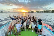 A group of people is posing for a photo on a boat with a beautiful sunset in the background.