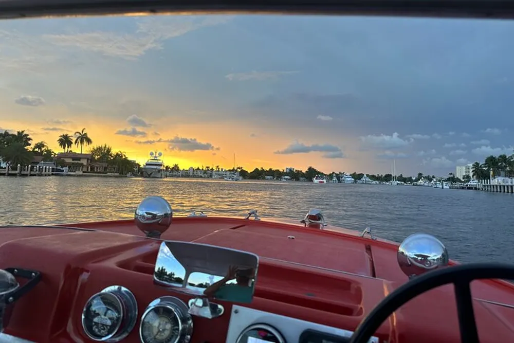 A view from a classic boat with a red dashboard cruising through a canal at sunset under a partly cloudy sky
