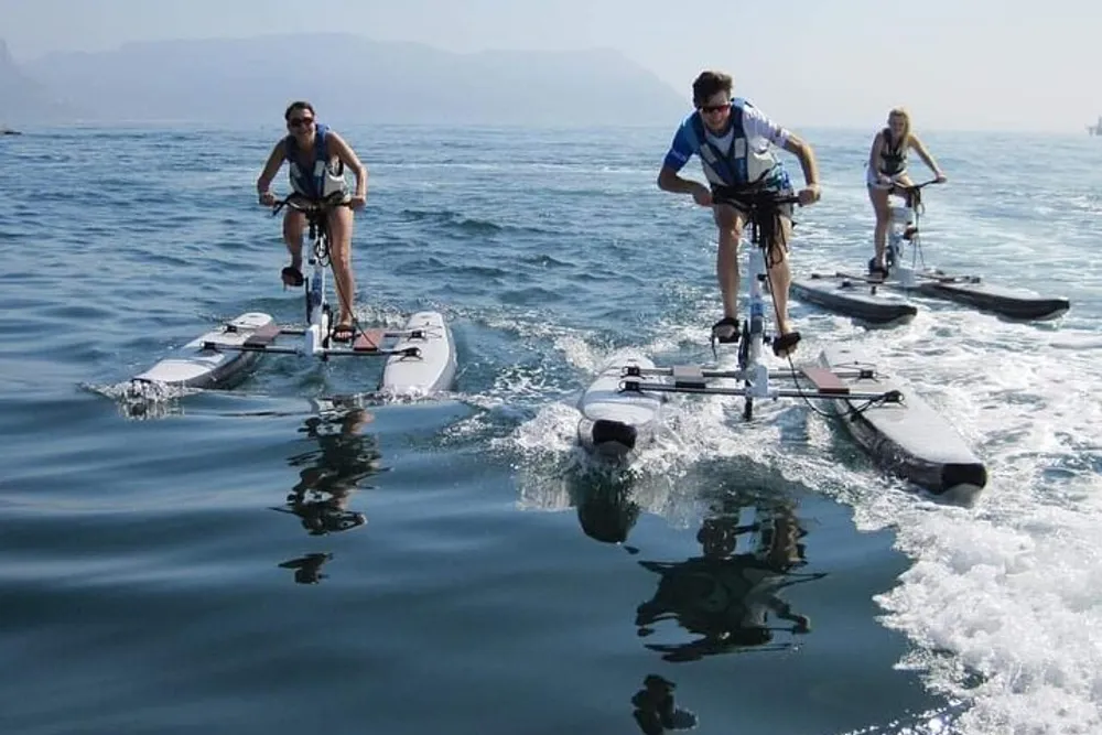 Three people are riding water bikes across a calm sea surface