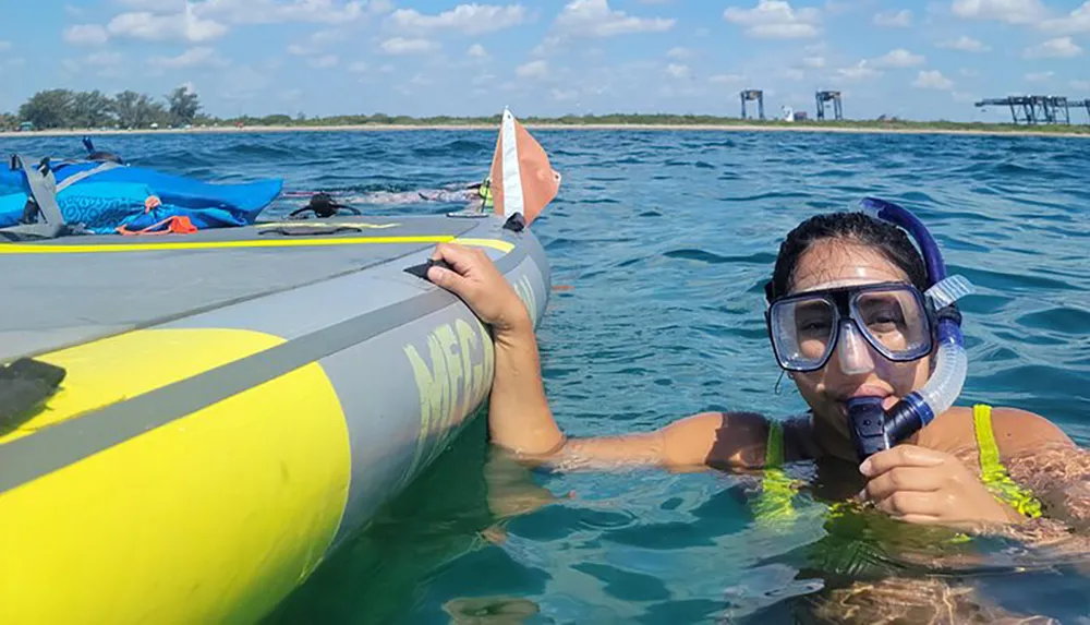 A person wearing snorkeling gear is holding onto a kayak in clear blue water