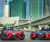 Two Polaris Slingshot three-wheeled vehicles are parked on an urban road with skyscrapers and a bridge in the background