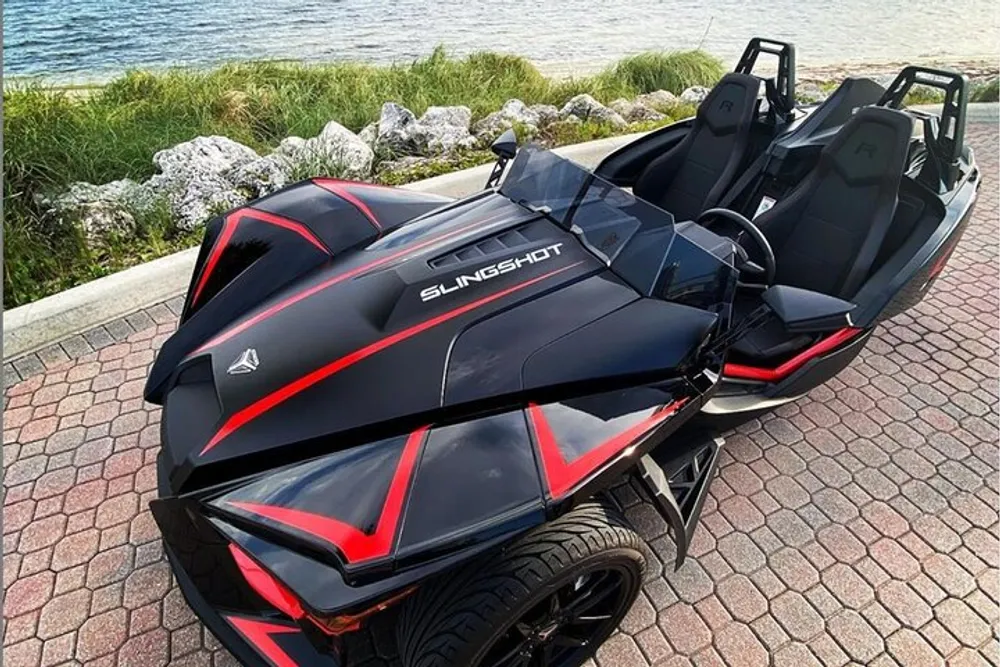The image shows a Polaris Slingshot a three-wheeled motor vehicle with its open cockpit and two seats parked near a waterside area
