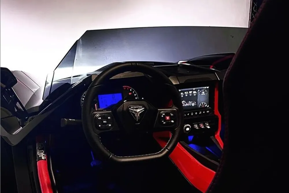 This image shows the interior view from the drivers seat of a modern vehicle featuring a sleek dashboard multi-functional steering wheel and digital displays with red accents on the doors and center console