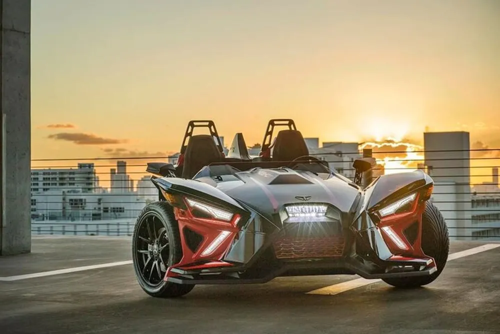 A Polaris Slingshot an open-air three-wheeled vehicle is parked on a rooftop at sunset with the city skyline in the background