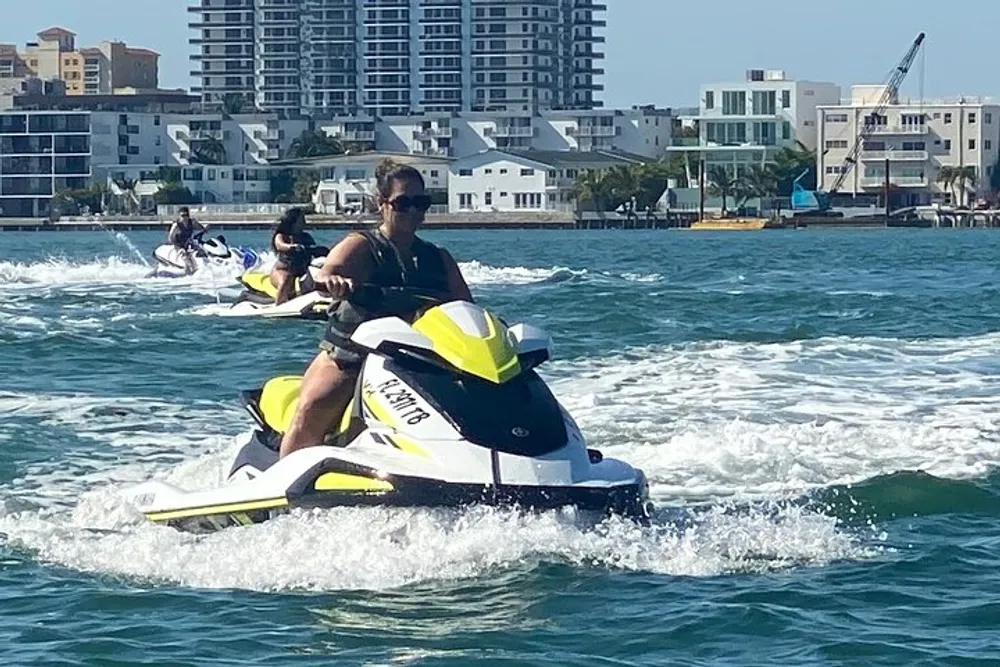 People are riding jet skis on the water with a backdrop of coastal city buildings