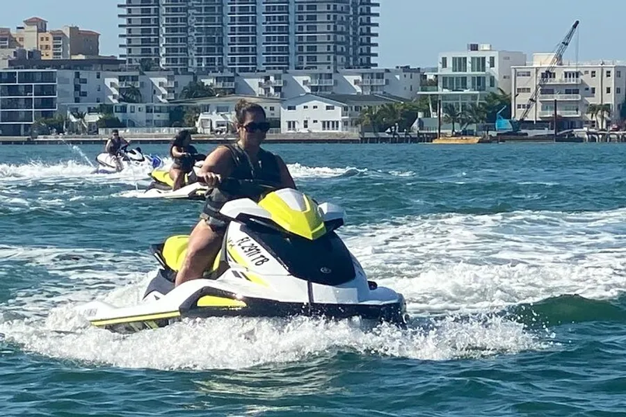 People are riding jet skis on the water with a backdrop of coastal city buildings.
