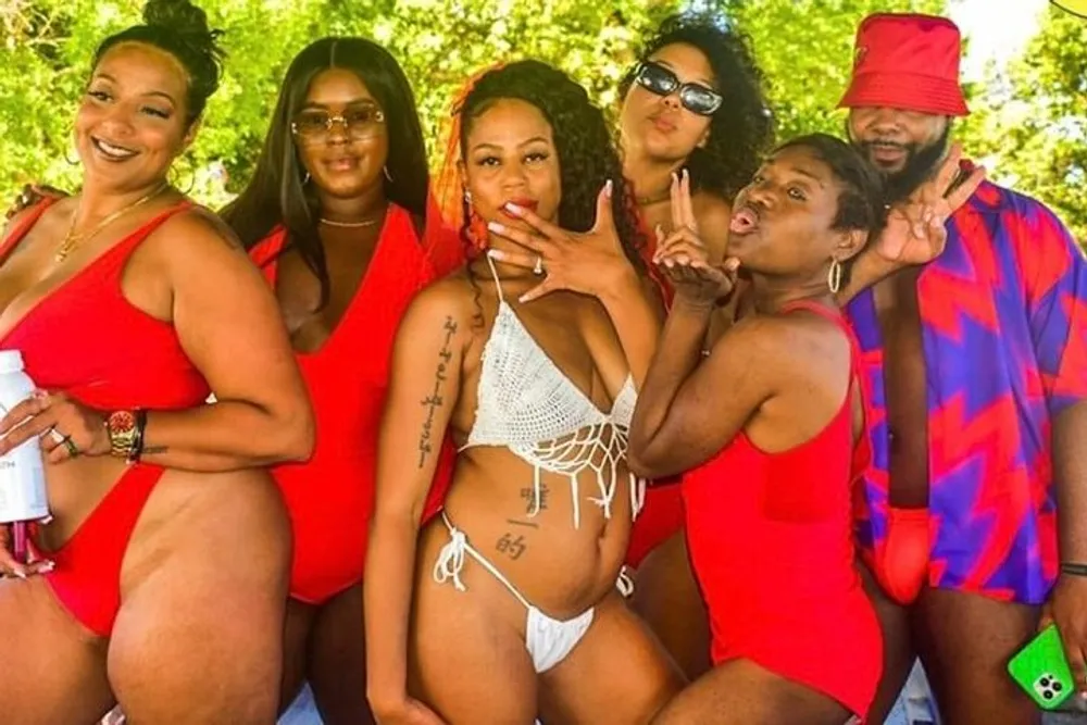 A group of six women and one man are posing enthusiastically in swimwear with most wearing red creating a lively and coordinated appearance