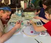 Two individuals are engaged in painting on oval-shaped canvases at a table adorned with painting supplies exhibiting a creative and enjoyable activity