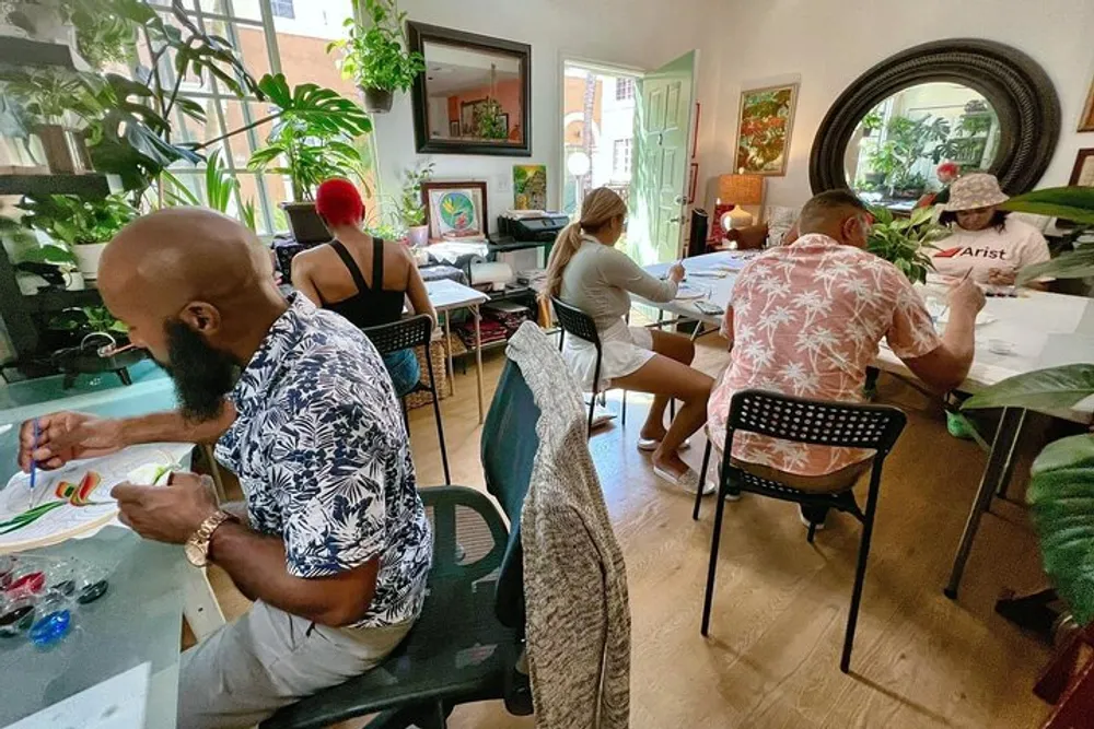 A group of people is engaged in an art workshop inside a cozy room filled with plants and colorful decor