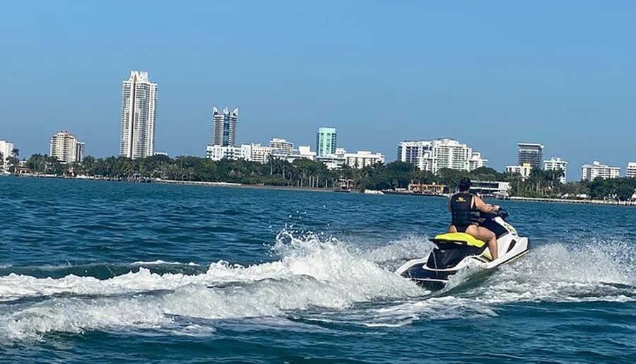A person is riding a jet ski on the water with a city skyline in the background.