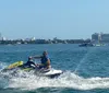 A person is riding a jet ski on a bright day with a city coastline visible in the background