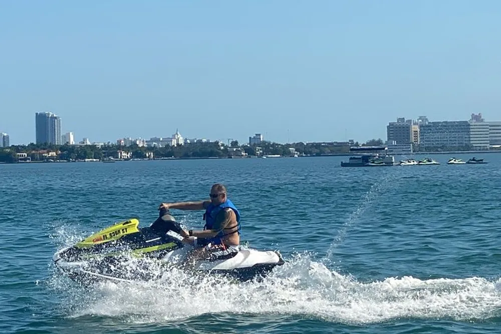 A person is riding a jet ski on a bright day with a city coastline visible in the background