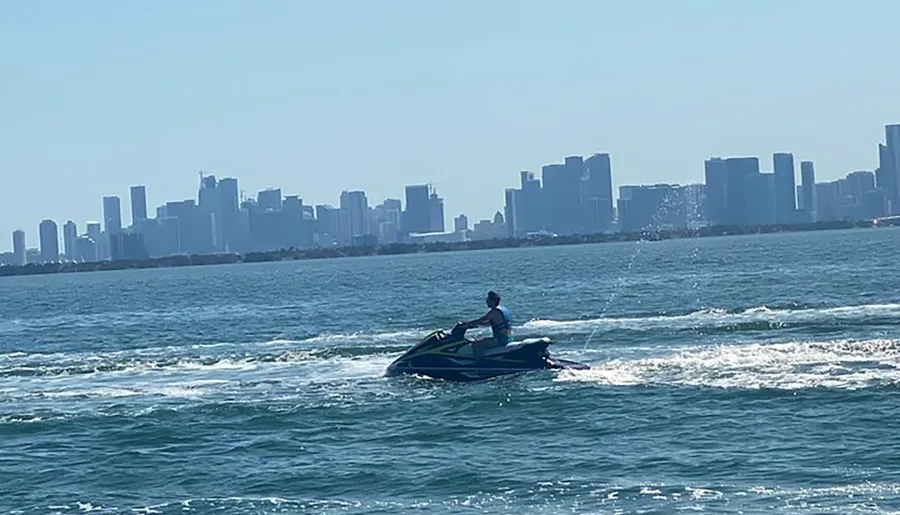 A person is riding a jet ski on the water with a city skyline in the background.