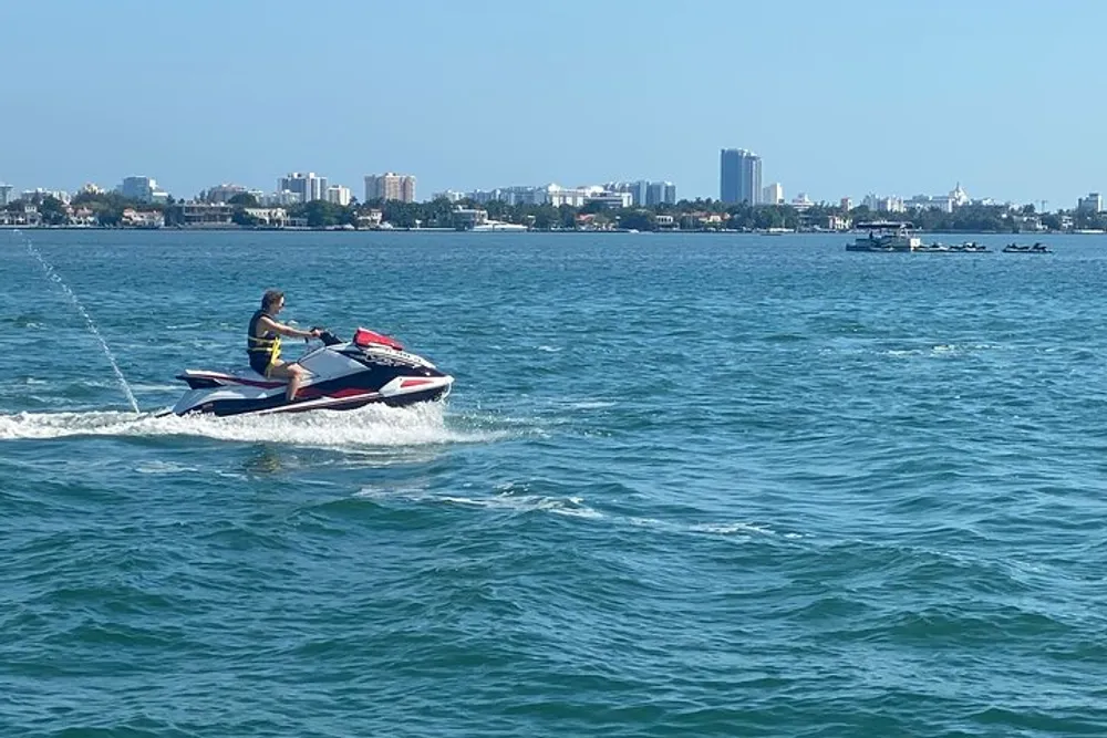 A person is riding a jet ski on a clear day with a city skyline in the background