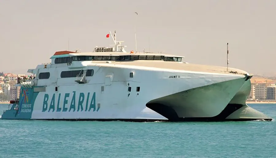 The image shows a large Balearia catamaran ferry named Jaume II on the water near a coastal city.