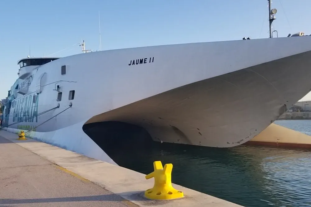 The image shows the bow of a large white ship named JAUME II docked at a quay with a yellow mooring bollard in the foreground