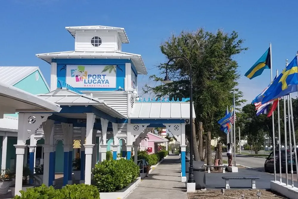 The image shows the Port Lucaya Marketplace in a tropical setting with bright blue skies Bahamian flags and pastel-colored buildings