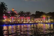 A waterfront building adorned with colorful lights is reflected in the water at night, creating a vibrant and festive atmosphere.