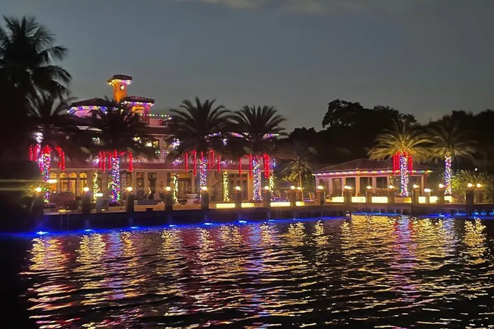 A waterfront building adorned with colorful lights is reflected in the water at night creating a vibrant and festive atmosphere