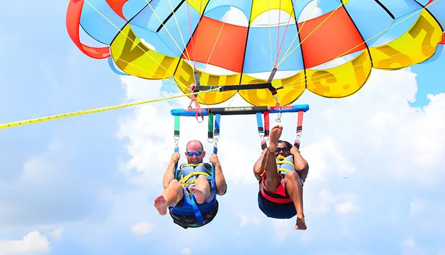 Two people are enjoying a parasailing adventure in a clear blue sky.