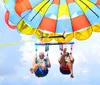 Two people are enjoying a parasailing adventure against a scenic backdrop of blue skies and fluffy white clouds
