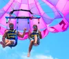 Two people are enjoying a parasailing adventure against a scenic backdrop of blue skies and fluffy white clouds