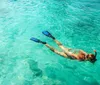 A person is snorkeling in clear turquoise water wearing blue fins and an orange snorkel