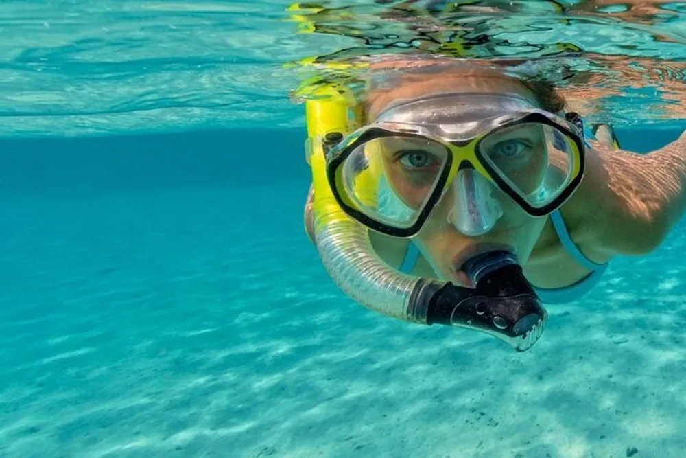 A person wearing a snorkeling mask and snorkel is partially submerged in clear blue water