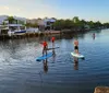 A group of people are paddleboarding on calm waters near a dock with houses and boats in the background during what appears to be late afternoon
