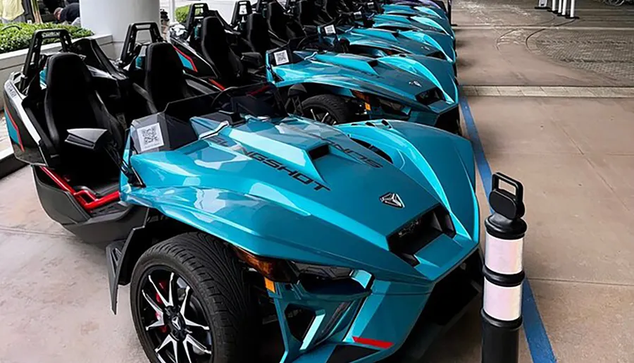 A lineup of turquoise Polaris Slingshot three-wheeled vehicles is displayed outdoors, potentially ready for rental or a group event.