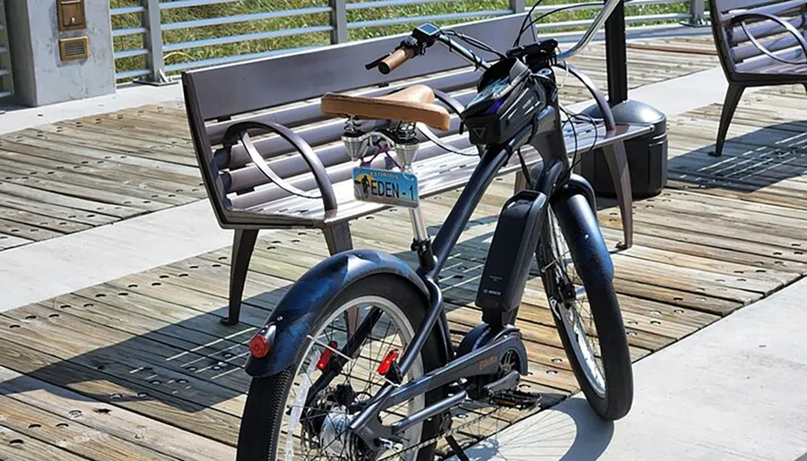 An electric bicycle is parked on a wooden deck next to a bench, under bright daylight.