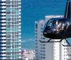 A helicopter with passengers is flying close to high-rise buildings near a beachfront