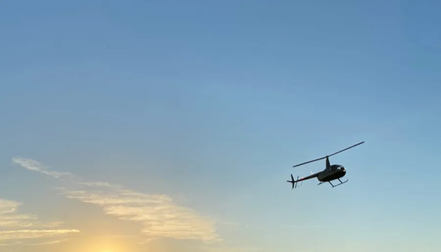 A helicopter is flying in a clear sky with the setting sun in the background.