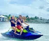 Two people are enjoying a jet ski ride on a sunny day with waterfront houses in the background