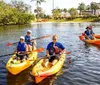 A group of people are enjoying a sunny day kayaking on a calm waterway lined with lush greenery and palm trees
