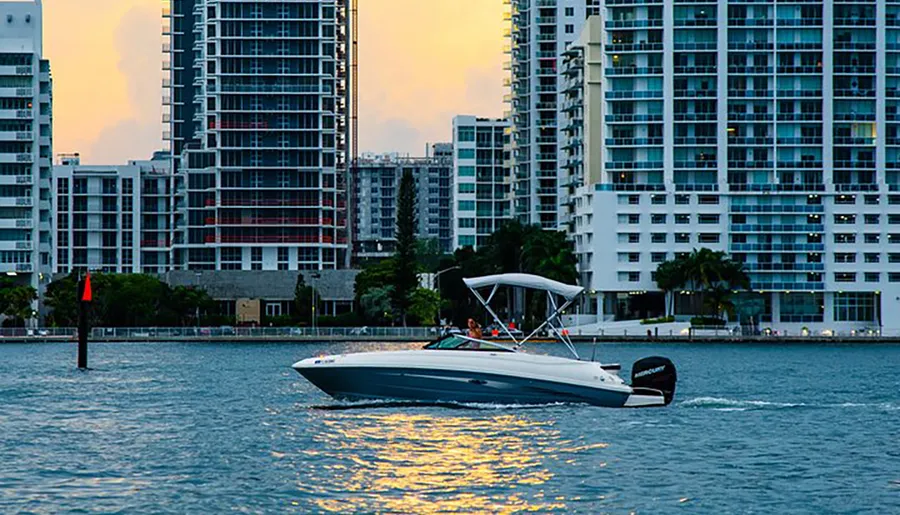A boat is cruising on the water with a backdrop of modern high-rise buildings in the twilight hours.