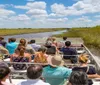 A group of tourists is enjoying an airboat tour through a grass-lined waterway under a clear blue sky