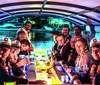 A group of people wearing captains hats and festive leis are enjoying a social gathering on a boat with an illuminated table at night