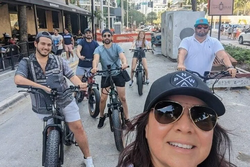 A group of people poses for a selfie while riding bicycles on an urban street