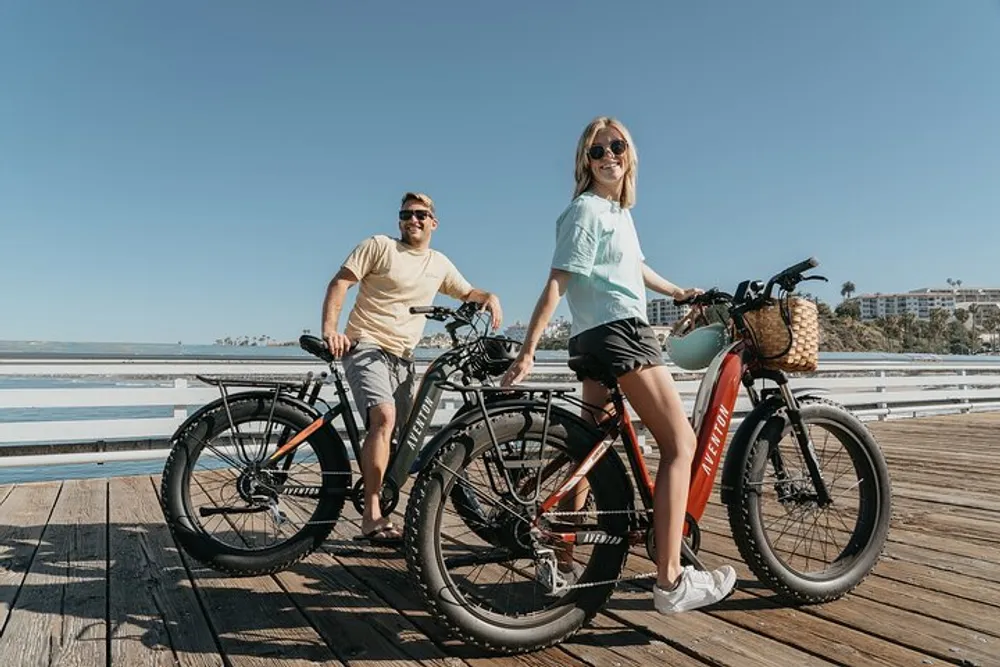 A man and a woman are standing with their bicycles on a sunny boardwalk by the sea