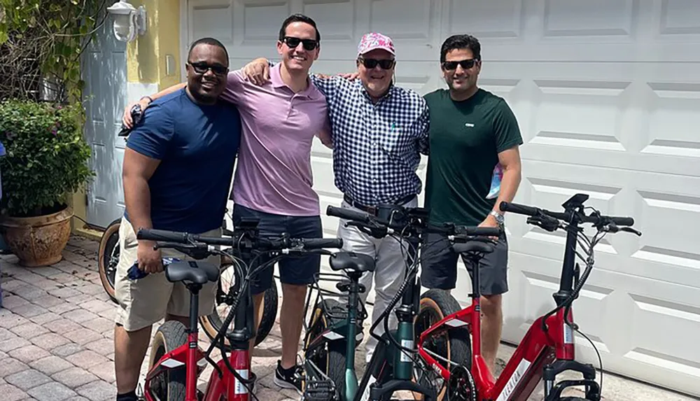 Four people are standing together in front of a garage with bicycles in front of them smiling at the camera